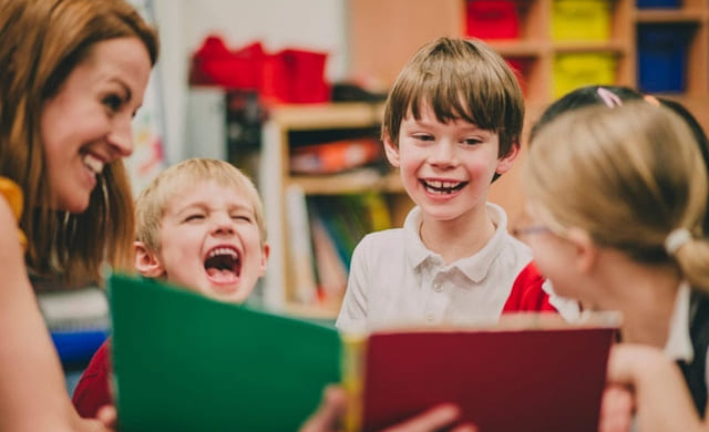 Lærer og elever ser sammen i en bok og smiler til hverandre.
